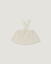 A light cream-colored linen dress with shoulder straps, laid flat against a neutral light gray background.