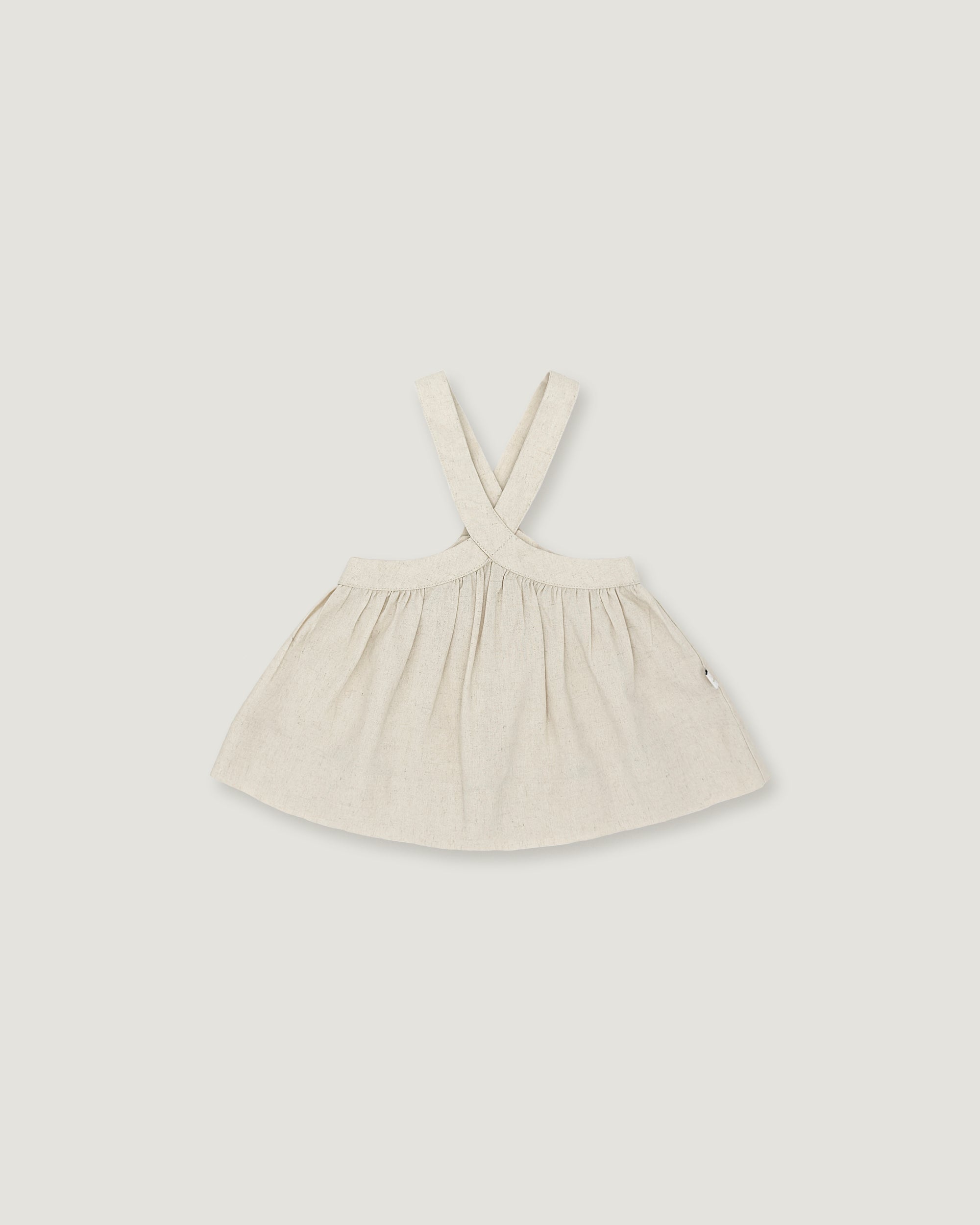 A light cream-colored linen dress with shoulder straps, laid flat against a neutral light gray background.