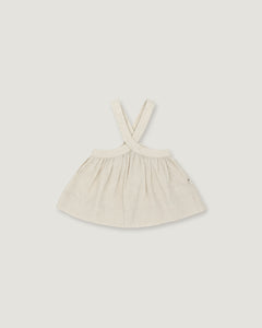 A light cream-colored linen dress with shoulder straps, laid flat against a neutral light gray background.