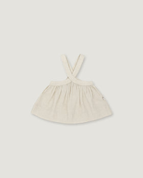 A light cream-colored linen dress with shoulder straps, laid flat against a neutral light gray background.