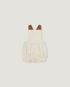 A baby romper in a light oatmeal-beige linen-like fabric, featuring brown faux-leather shoulder straps, shown flat on a light gray background.