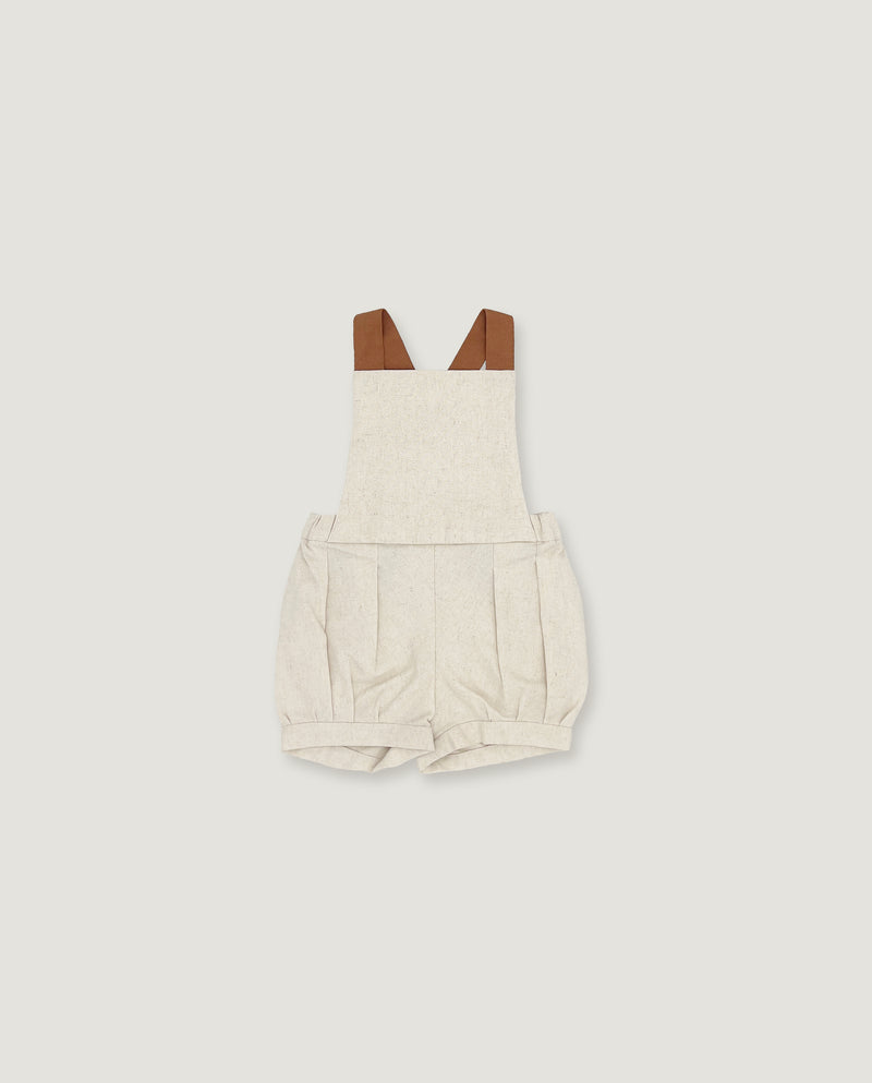 A baby romper in a light oatmeal-beige linen-like fabric, featuring brown faux-leather shoulder straps, shown flat on a light gray background.