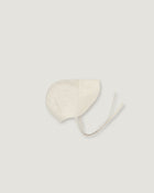 A light cream-colored fabric bonnet with long ties, photographed flat against a solid, very light gray background.