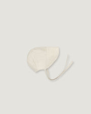 A light cream-colored fabric bonnet with long ties, photographed flat against a solid, very light gray background.