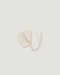 A cream-colored cotton bonnet with tie strings, photographed flat against a solid light gray background.