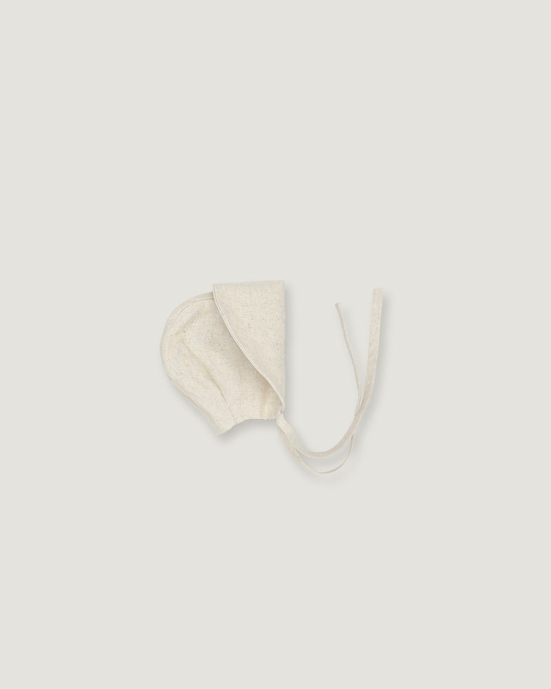 A cream-colored cotton bonnet with tie strings, photographed flat against a solid light gray background.