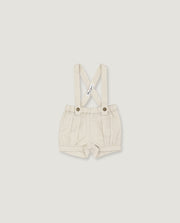 A pair of baby boy's cream-colored linen suspenders shorts with adjustable shoulder straps and metal snap buttons, shown flat on a light gray background.