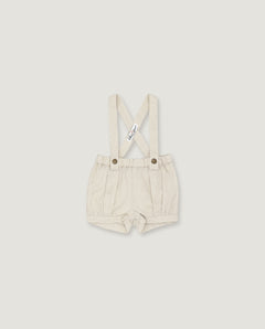 A pair of baby boy's cream-colored linen suspenders shorts with adjustable shoulder straps and metal snap buttons, shown flat on a light gray background.