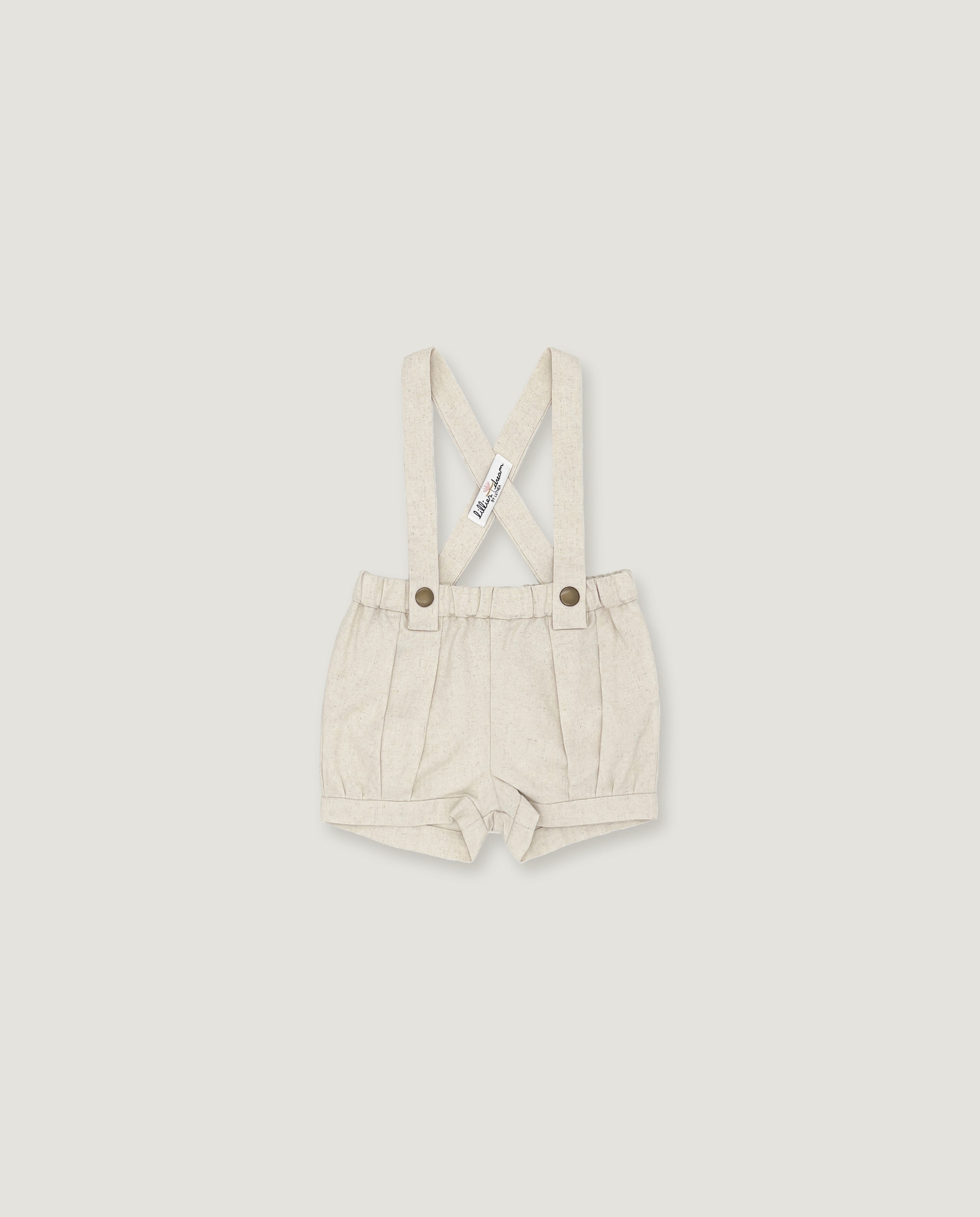 A pair of baby boy's cream-colored linen suspenders shorts with adjustable shoulder straps and metal snap buttons, shown flat on a light gray background.