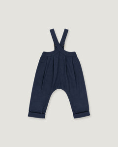 A pair of baby boy's navy blue suspenders with a unique curved leg design and cuffed hems, shown flat on a light gray background.