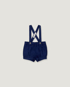 A pair of navy blue baby boy shorts with adjustable suspenders, featuring a white fabric brand tag and gold-tone snap buttons, displayed flat against a light gray background.