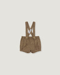 A pair of toddler boy's linen suspender shorts in a warm brownish-beige color, featuring adjustable shoulder straps with a crossed design and a white brand tag.