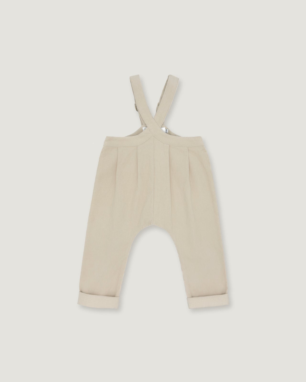 A pair of baby trousers in a light cream or beige color, featuring a bib-style waistband with adjustable shoulder straps and cuffed legs, shown flat against a light gray background.
