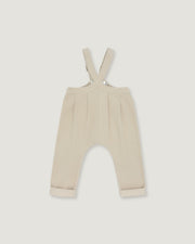 A pair of baby trousers in a light cream or beige color, featuring a bib-style waistband with adjustable shoulder straps and cuffed legs, shown flat against a light gray background.