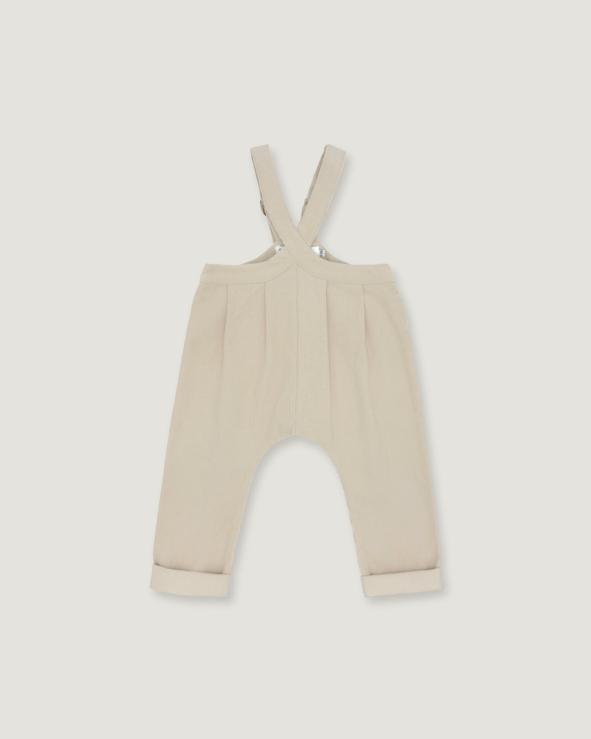 A pair of baby trousers in a light cream or beige color, featuring a bib-style waistband with adjustable shoulder straps and cuffed legs, shown flat against a light gray background.
