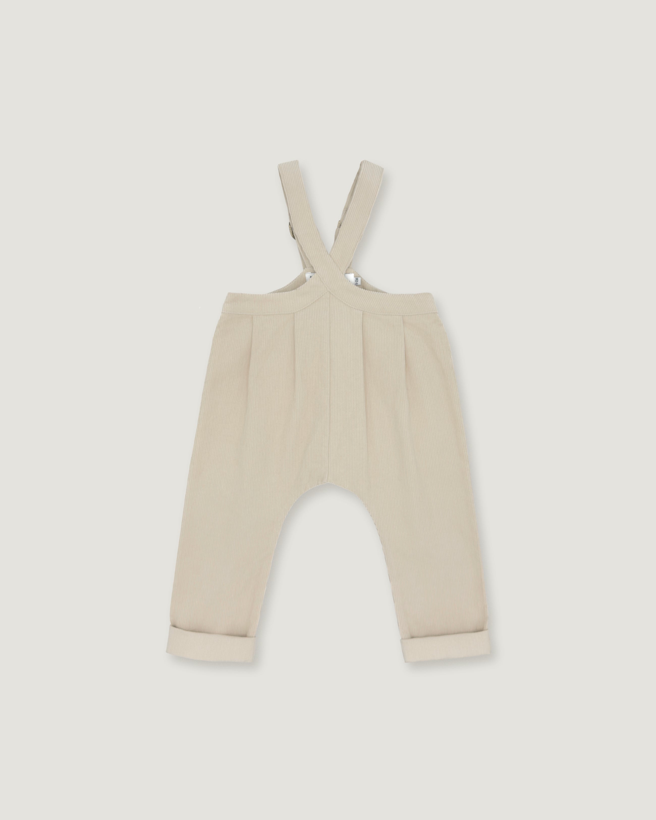 A pair of baby trousers in a light cream or beige color, featuring a bib-style waistband with adjustable shoulder straps and cuffed legs, shown flat against a light gray background.
