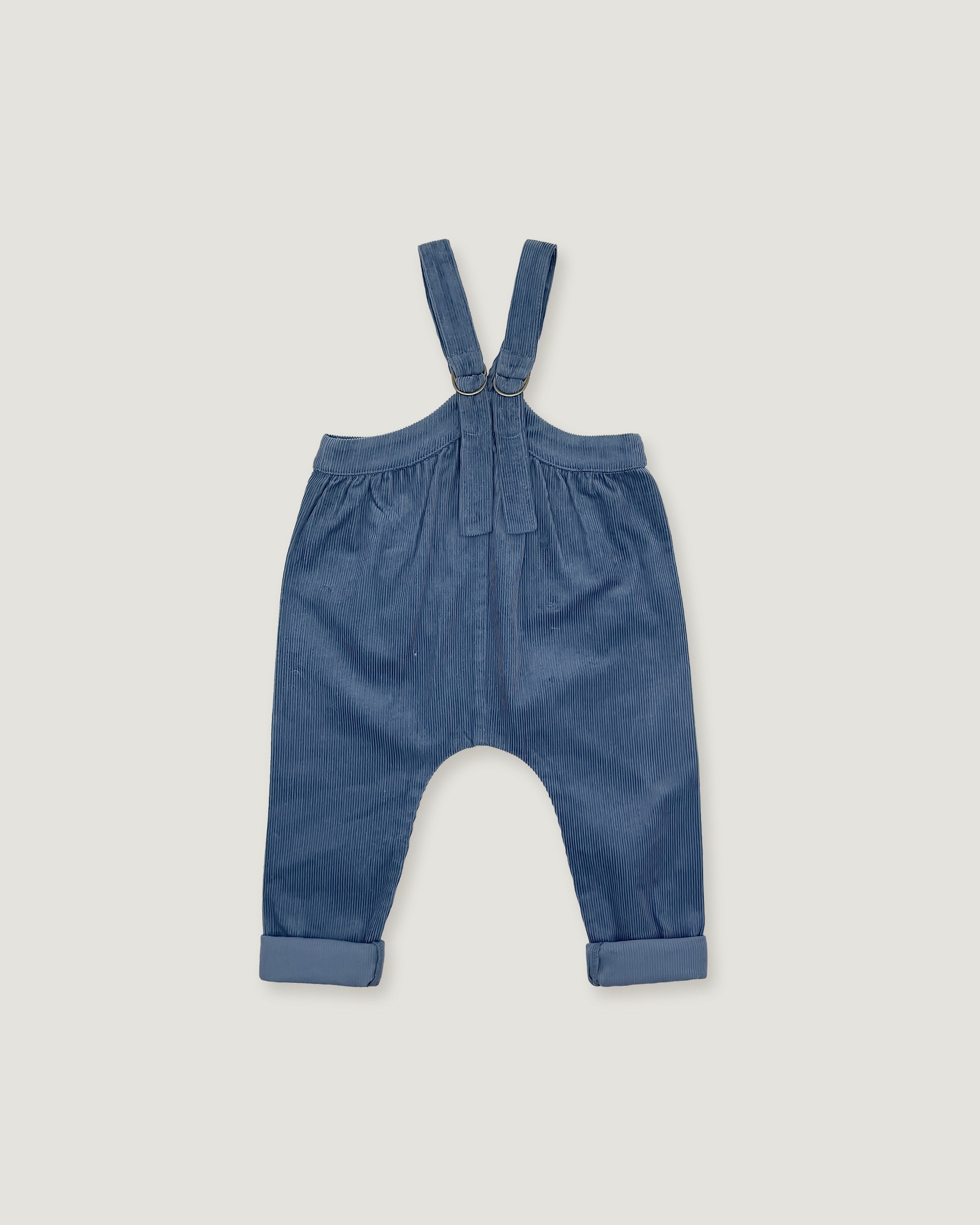 A pair of baby boy's blue corduroy suspenders with a button closure at the waist and rolled cuffs, laid flat on a light gray background.