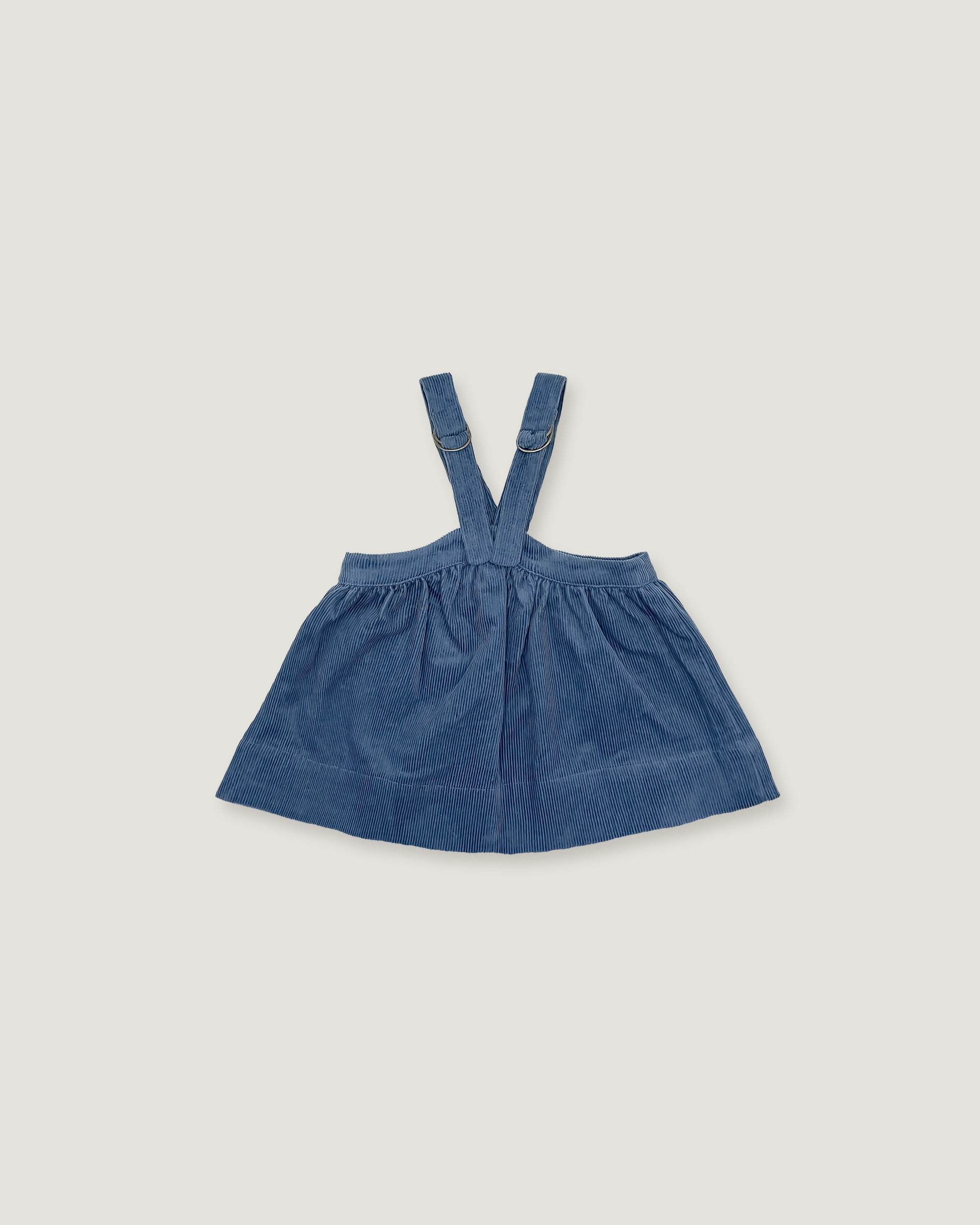 A blue denim baby dress with shoulder straps, laid flat on a light gray background.
