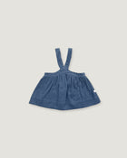 A baby girl's blue denim pinafore dress with shoulder straps, laid flat on a light gray background.
