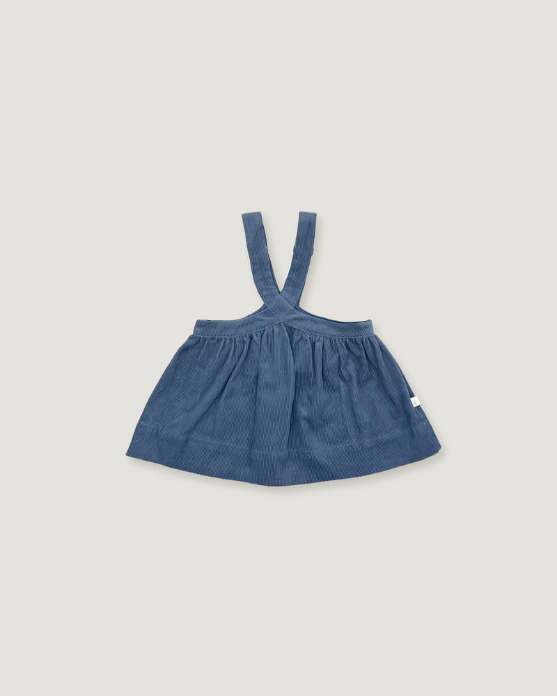 A baby girl's blue denim pinafore dress with shoulder straps, laid flat on a light gray background.