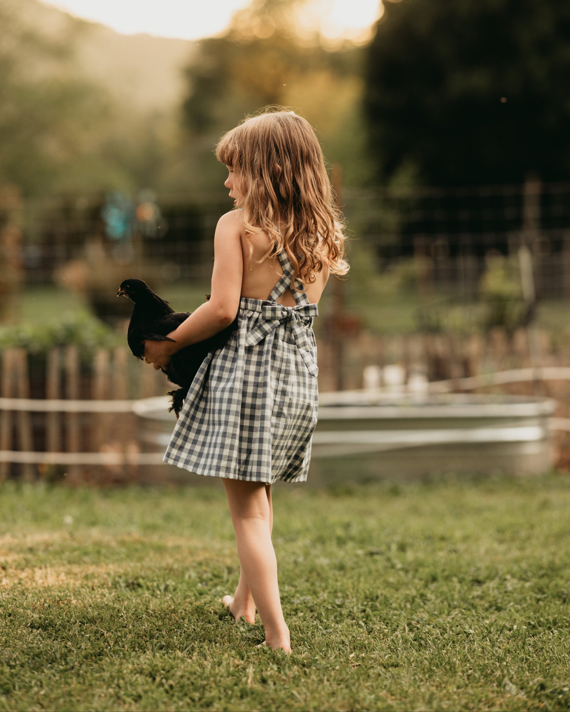 Back view of the model wearing a similar pinafore: The same 5-year-old model showcasing the back of the Slate Gingham pinafore, highlighting the strap design.
