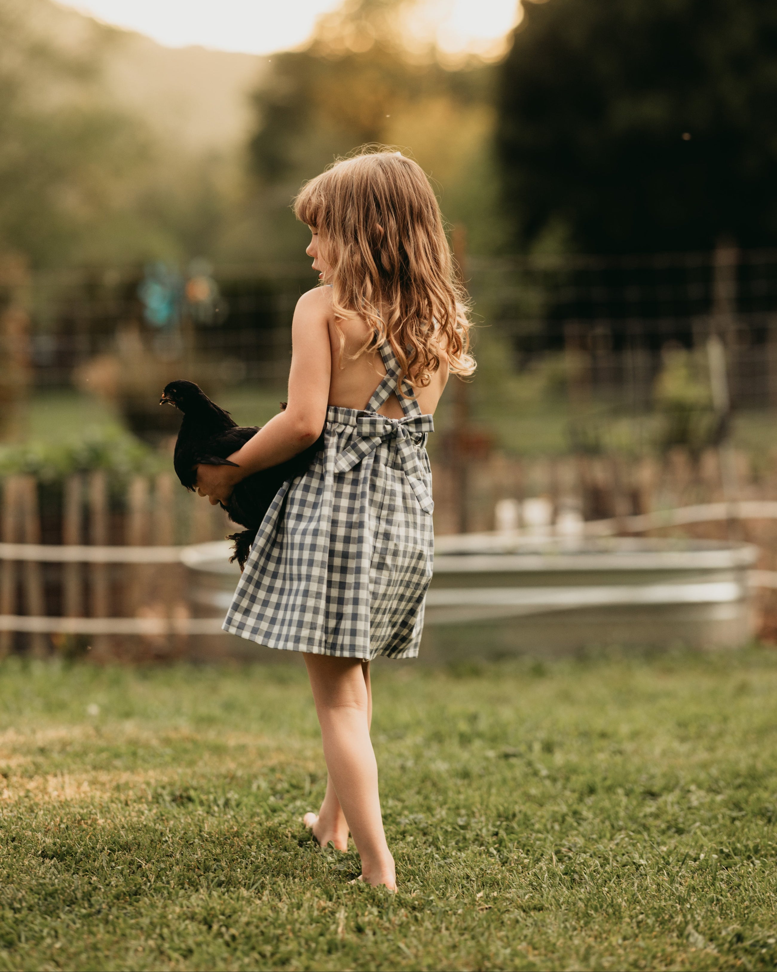Back view of the model wearing a similar pinafore: The same 5-year-old model showcasing the back of the Slate Gingham pinafore, highlighting the strap design.