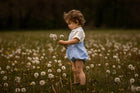 Child in a field of dandelions holding a dandelion seed head.