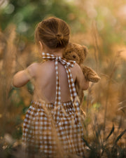 Model demonstrating alternative retro strap tying: A 3-year-old girl showing how to tie the straps of the Pinafore - Honey at the nape for a vintage-inspired look.