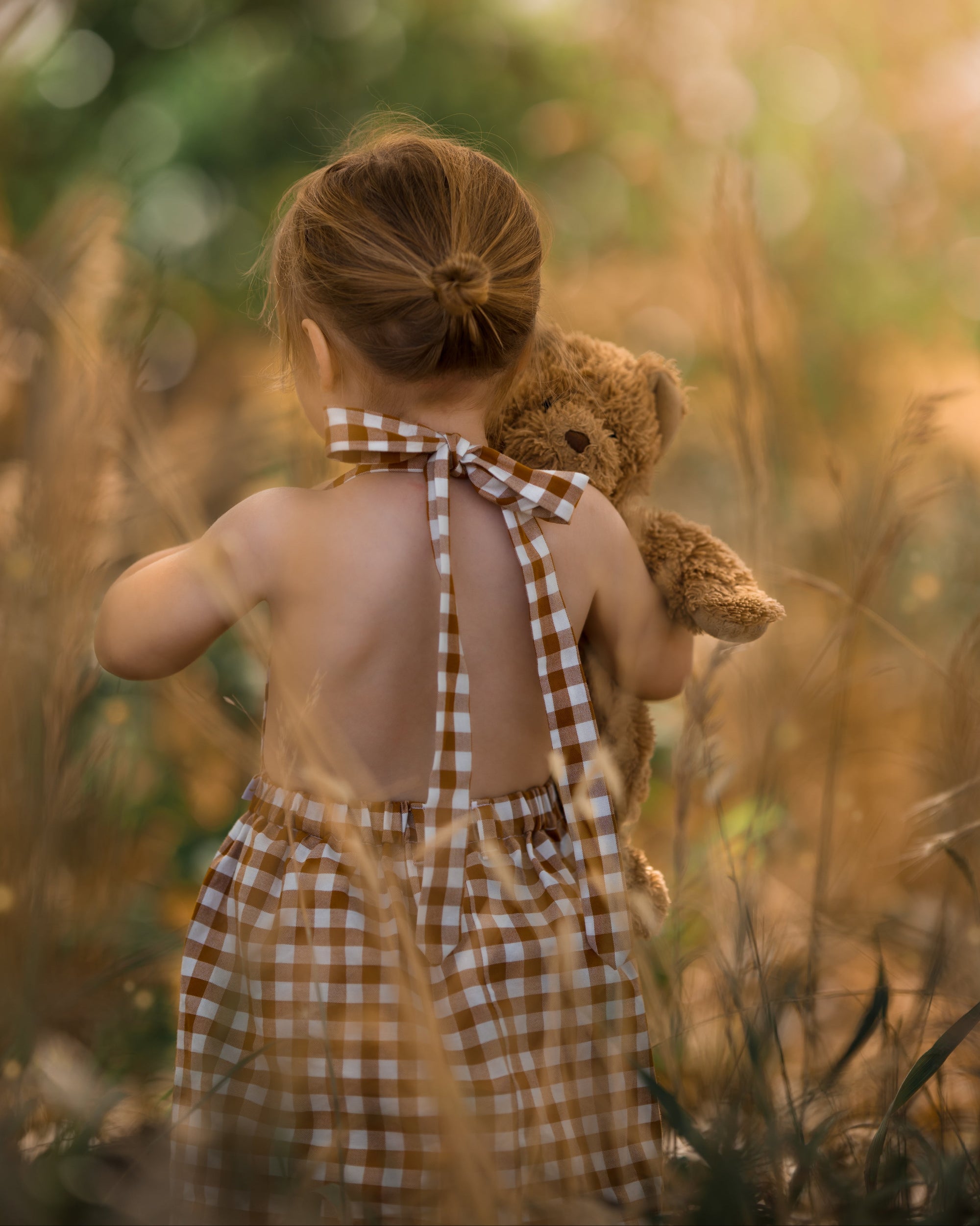 Model demonstrating alternative retro strap tying: A 3-year-old girl showing how to tie the straps of the Pinafore - Honey at the nape for a vintage-inspired look.