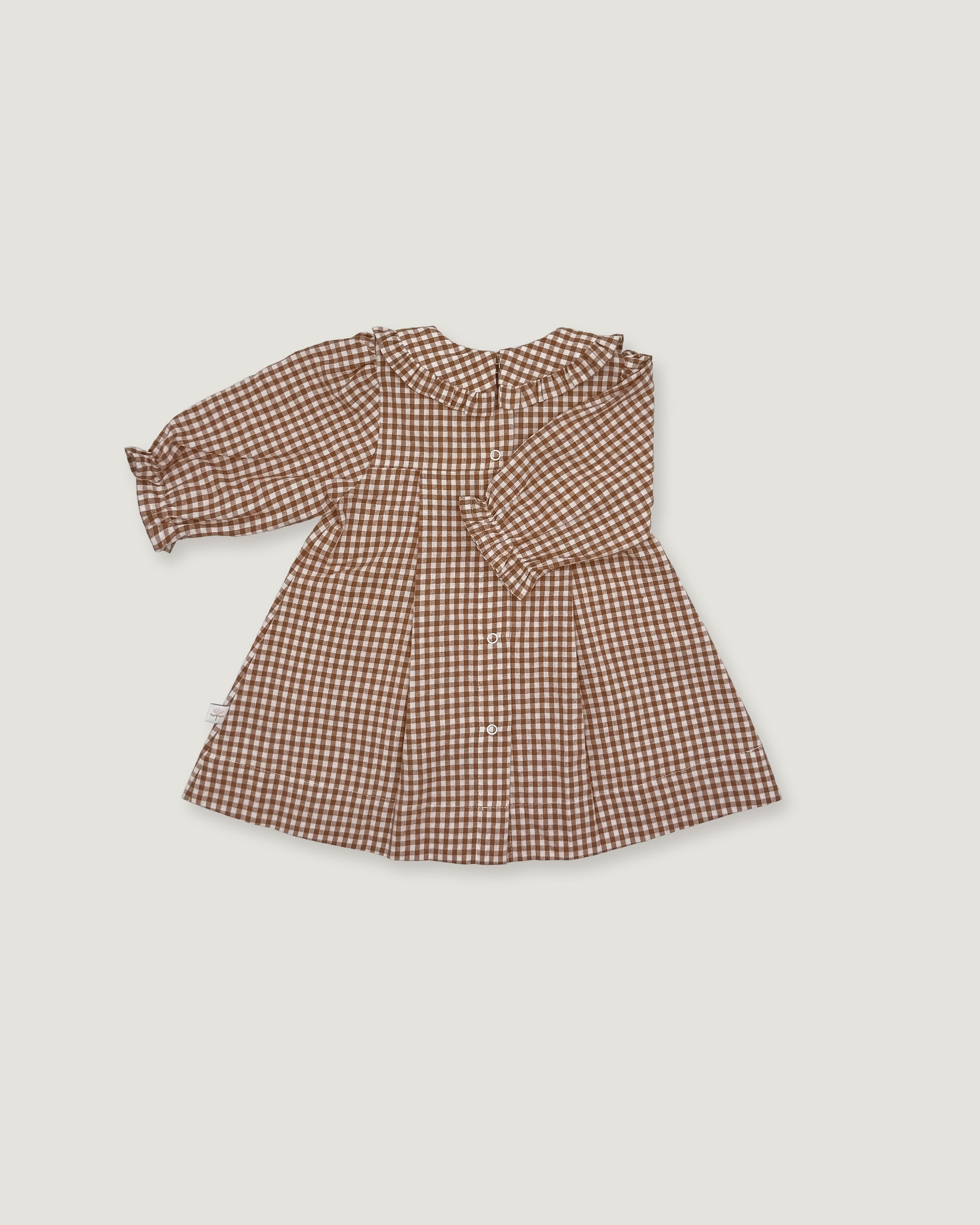 A long-sleeve baby dress with a brown and beige gingham pattern, featuring a ruffled collar and buttoned front, laid flat on a light gray background.