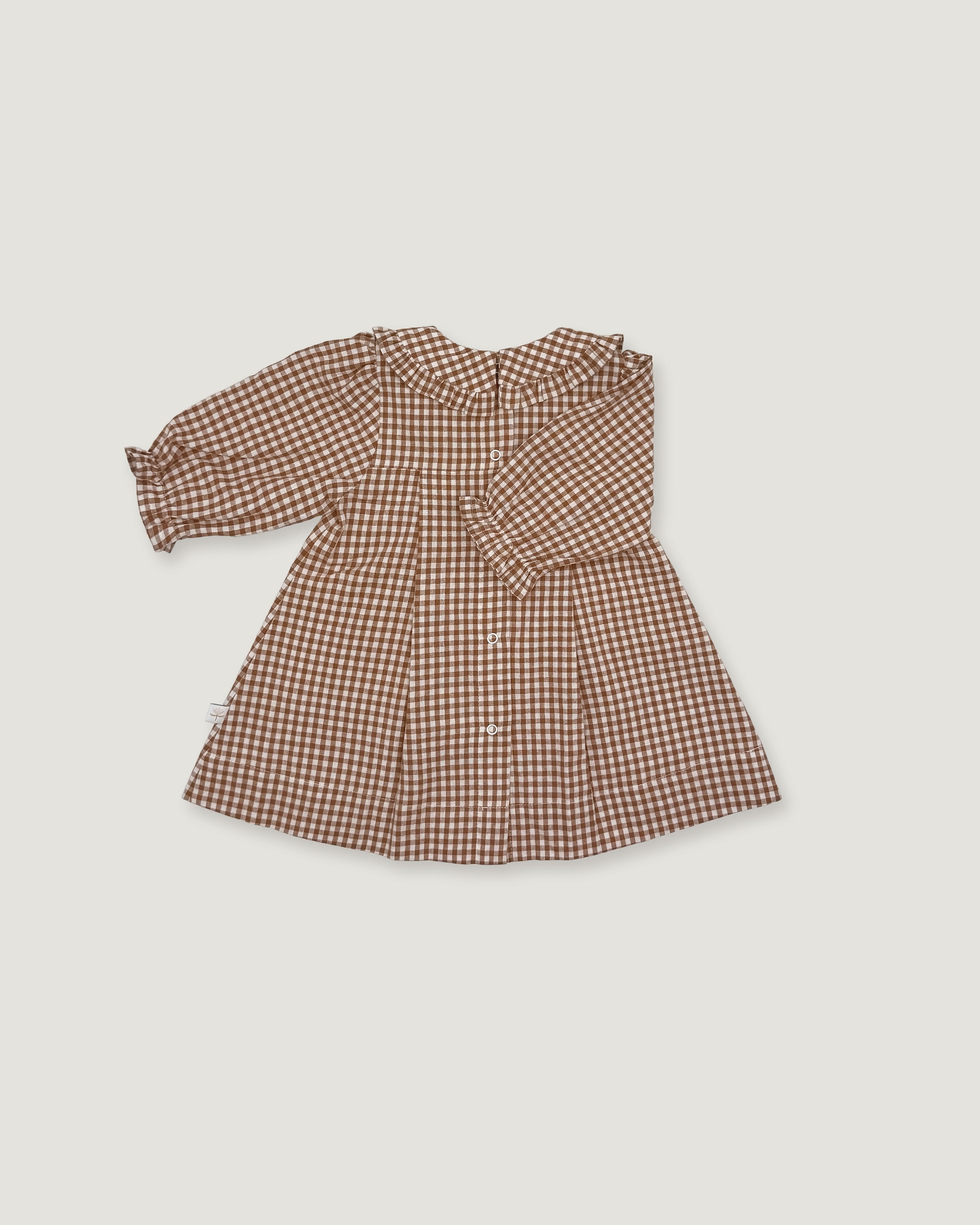 A long-sleeve baby dress with a brown and beige gingham pattern, featuring a ruffled collar and buttoned front, laid flat on a light gray background.