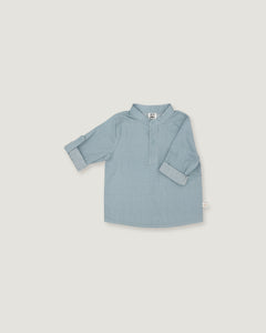 A light blue long-sleeve shirt for toddlers, featuring a polo-style collar and a short button placket, laid flat against a neutral light gray background.