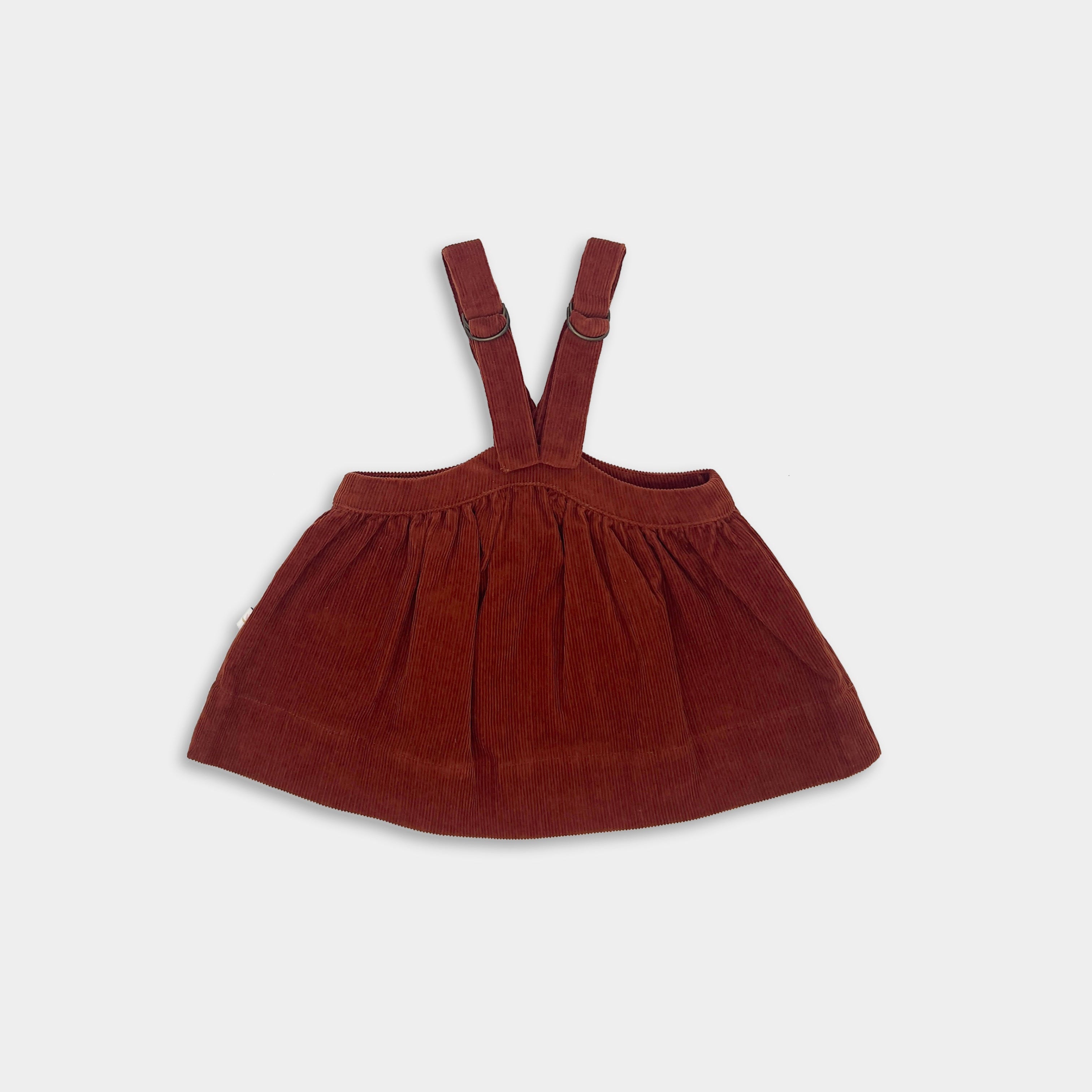 Brown red corduroy pinafore dress on a light gray background