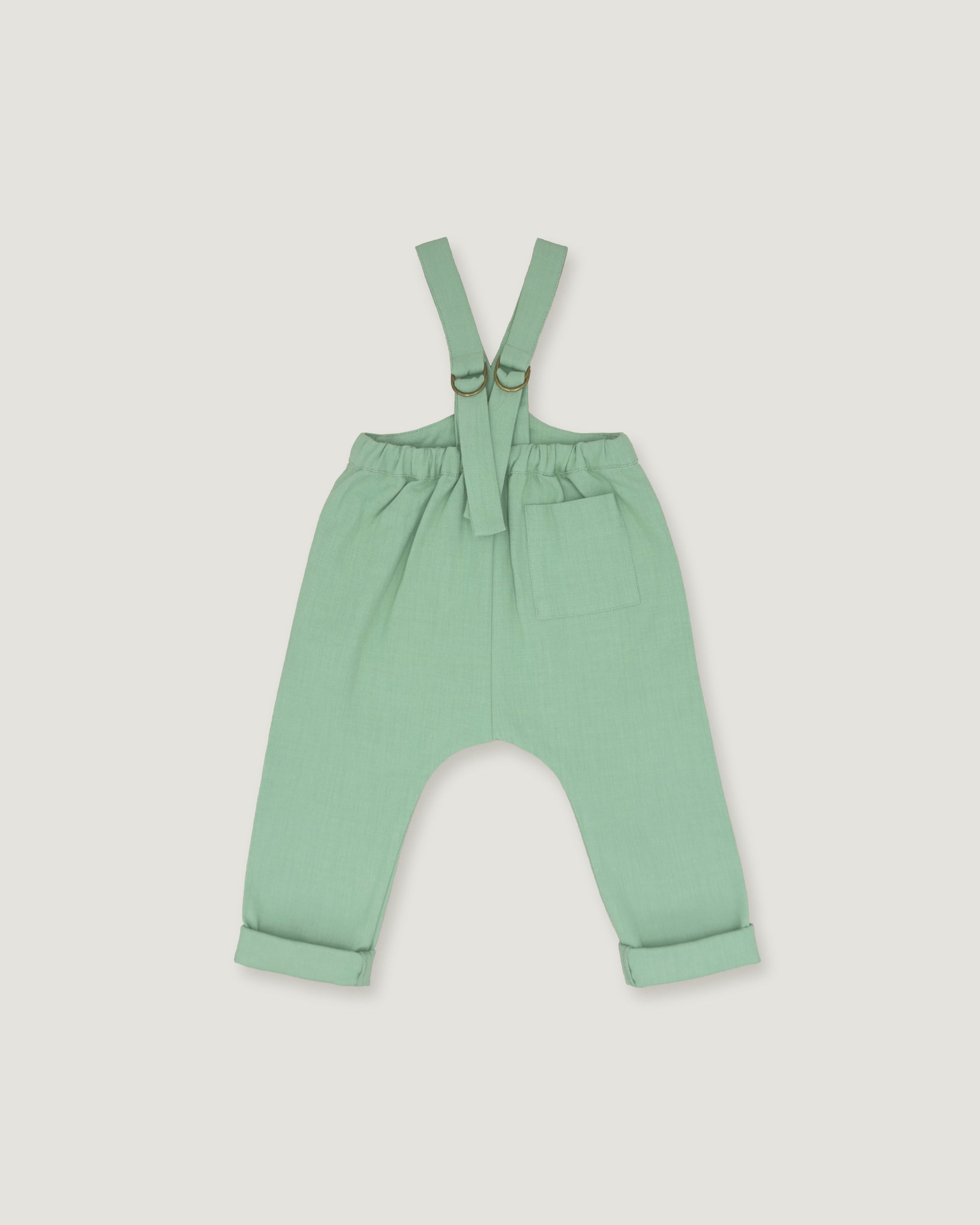 A pair of baby or toddler sage green suspenders with adjustable straps and a front pocket, laid flat on a light gray background.