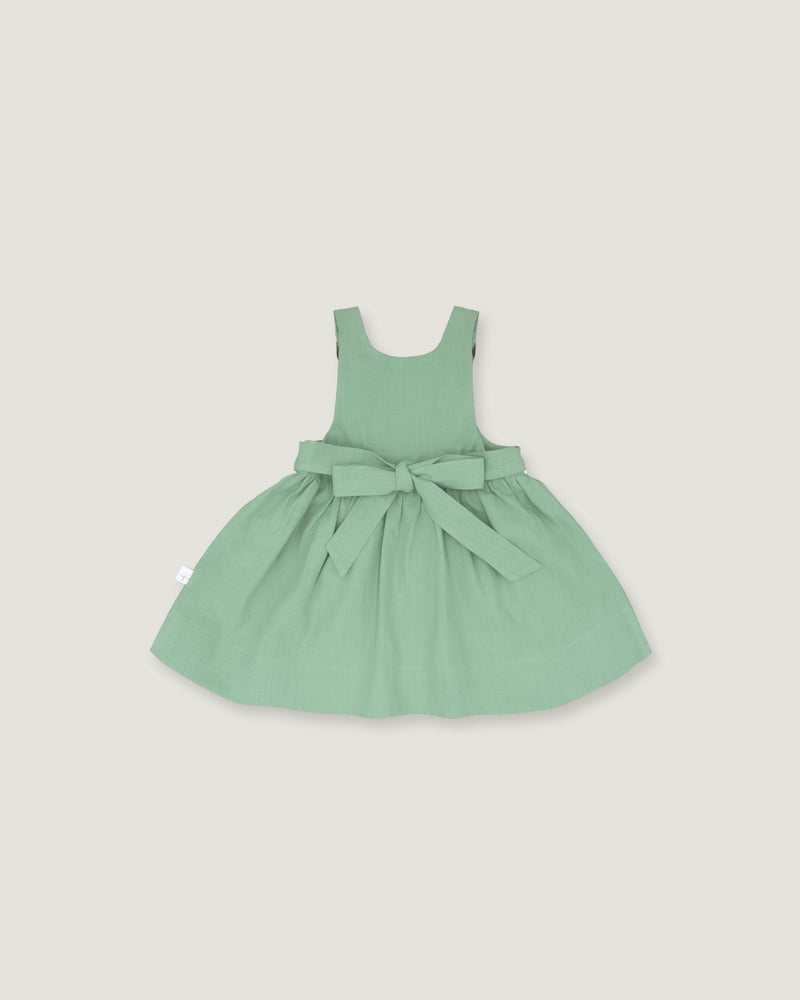 A light sage green sleeveless baby dress with a gathered skirt and a matching fabric bow at the waist, displayed flat against a solid light gray background.