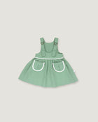 A sage green baby dress with white trim details, featuring a flared skirt and front pockets, shown against a solid light gray background.