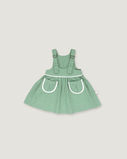 A sage green baby dress with white trim details, featuring a flared skirt and front pockets, shown against a solid light gray background.