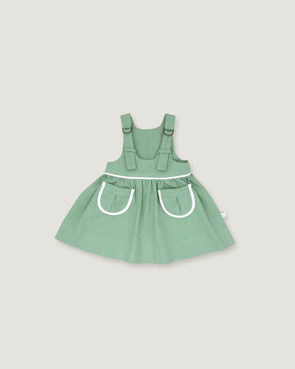 A sage green baby dress with white trim details, featuring a flared skirt and front pockets, shown against a solid light gray background.