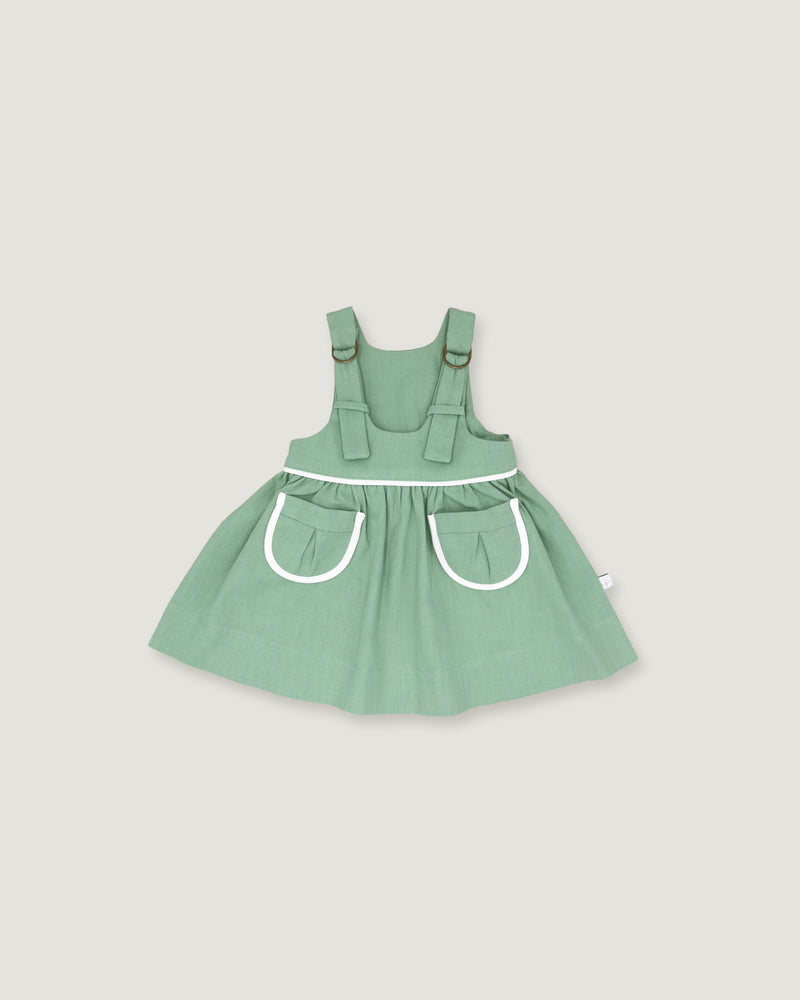 A sage green baby dress with white trim details, featuring a flared skirt and front pockets, shown against a solid light gray background.