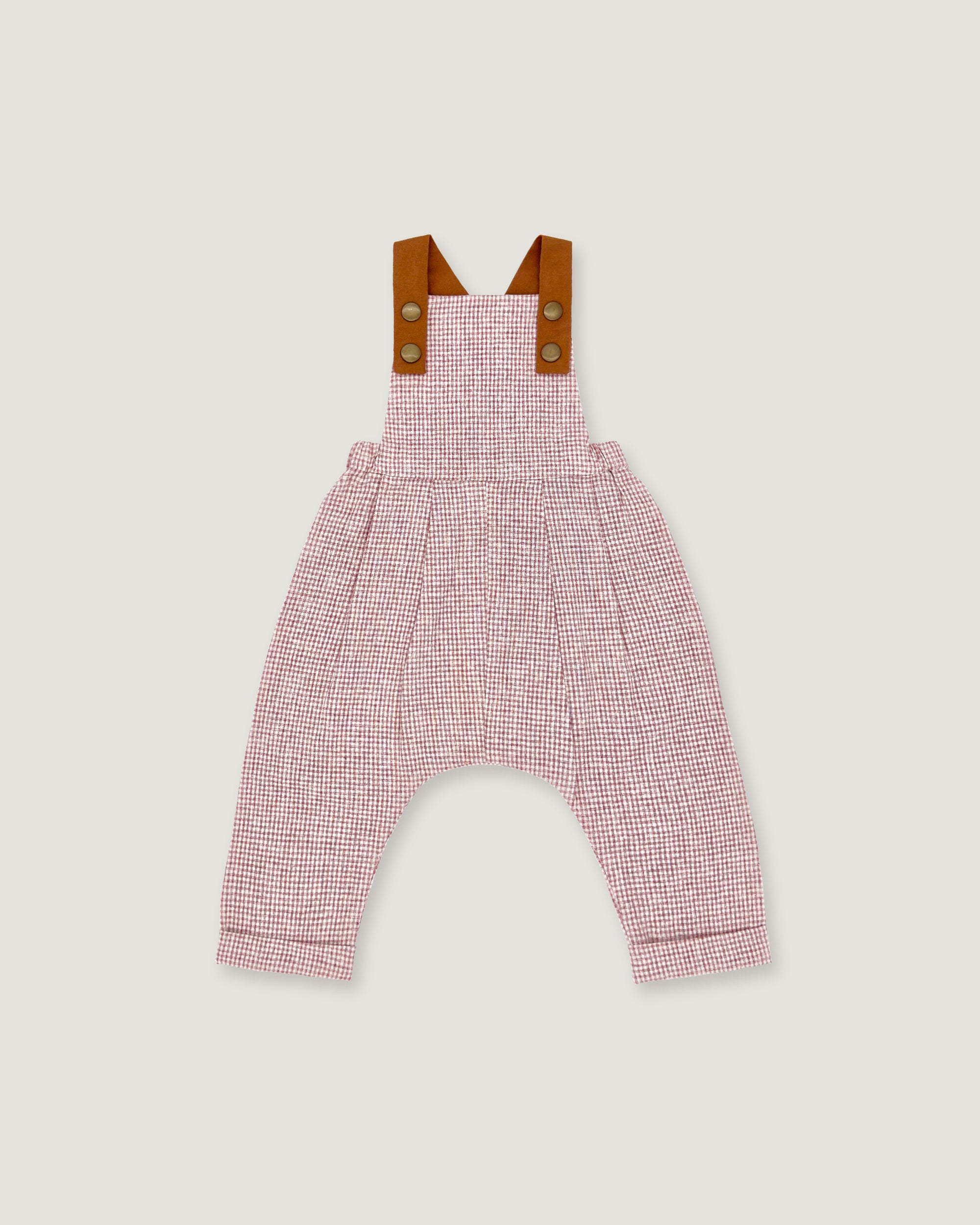 A baby romper with a pink and white micro-check pattern, featuring brown leather-like shoulder straps with snap buttons, shown flat on a light gray background.