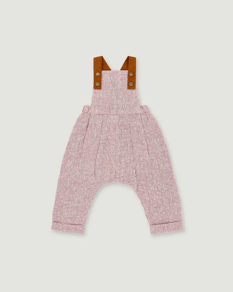 A baby romper with a pink and white micro-check pattern, featuring brown leather-like shoulder straps with snap buttons, shown flat on a light gray background.