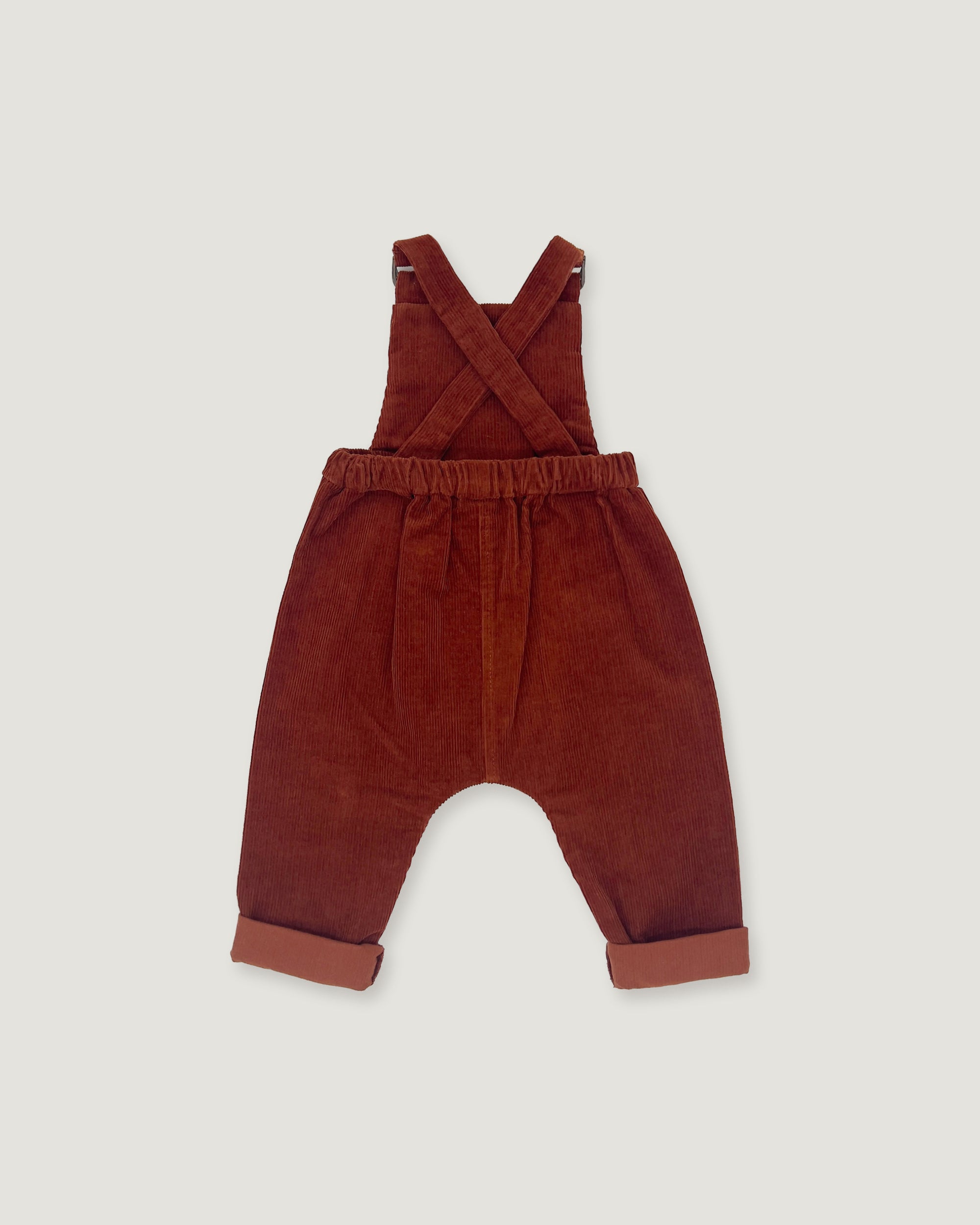 A pair of toddler corduroy bib overalls in a rust red color, featuring adjustable shoulder straps and rolled cuffs, shown flat on a light gray background.