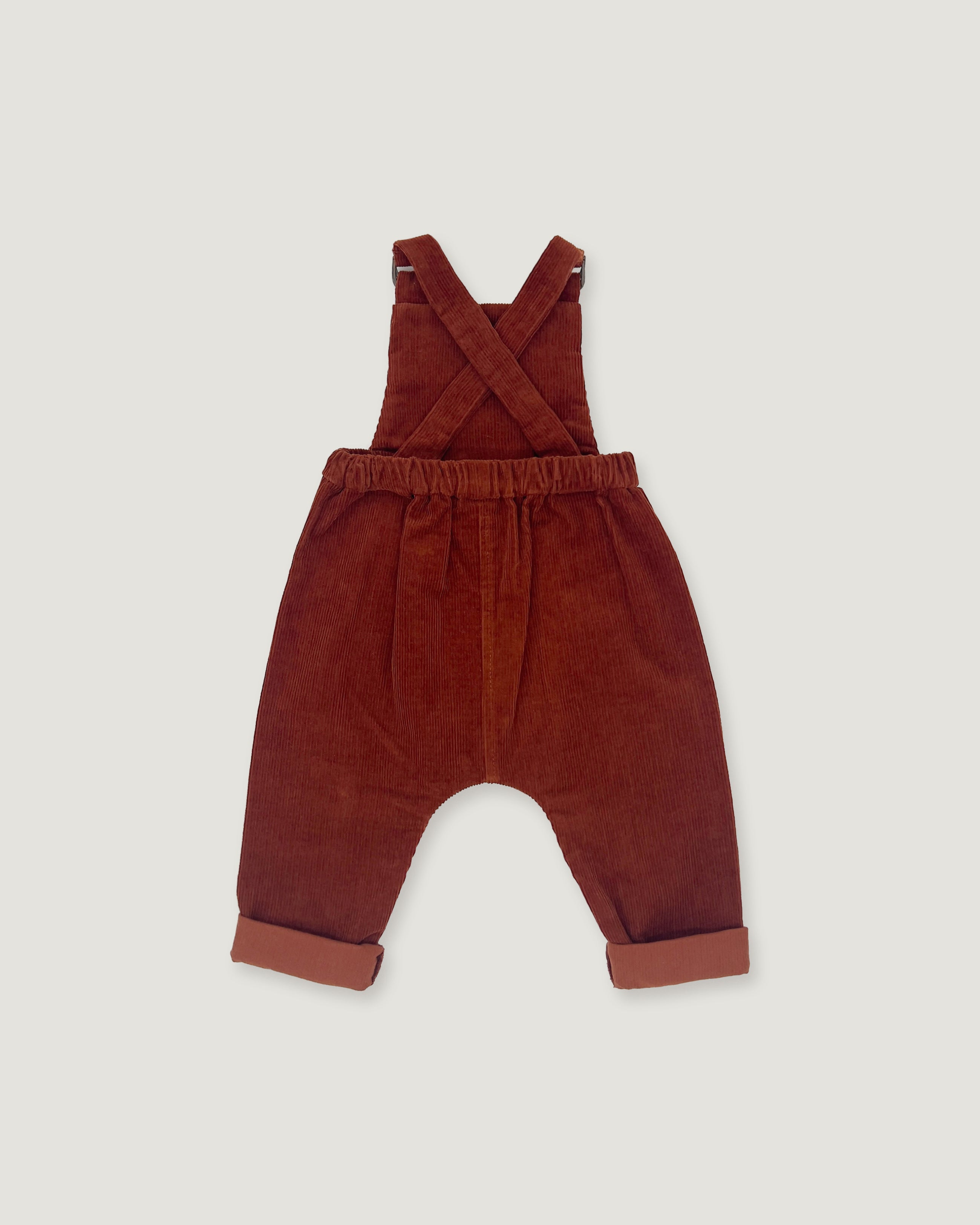 A pair of toddler corduroy bib overalls in a rust red color, featuring adjustable shoulder straps and rolled cuffs, shown flat on a light gray background.