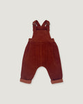 A pair of toddler corduroy bib overalls in a deep rust red color, featuring adjustable shoulder straps and cuffed harem-style legs, shown flat on a light gray background.