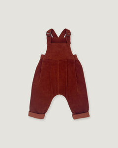 A pair of toddler corduroy bib overalls in a deep rust red color, featuring adjustable shoulder straps and cuffed harem-style legs, shown flat on a light gray background.