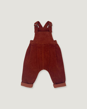A pair of toddler corduroy bib overalls in a deep rust red color, featuring adjustable shoulder straps and cuffed harem-style legs, shown flat on a light gray background.