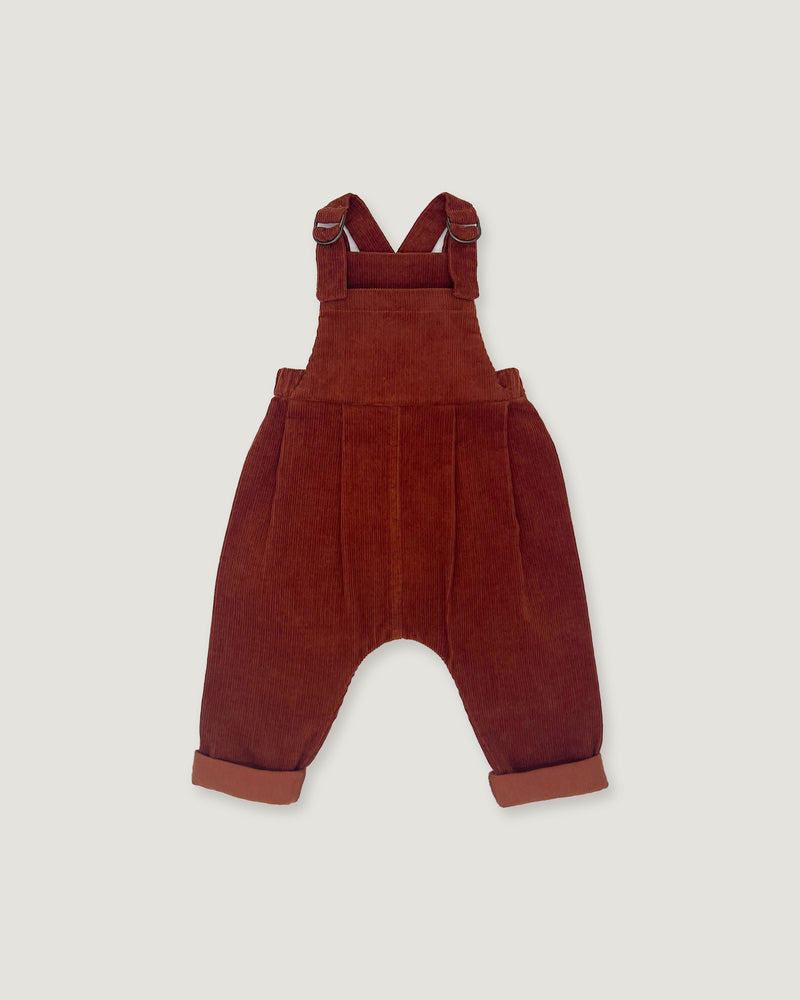 A pair of toddler corduroy bib overalls in a deep rust red color, featuring adjustable shoulder straps and cuffed harem-style legs, shown flat on a light gray background.