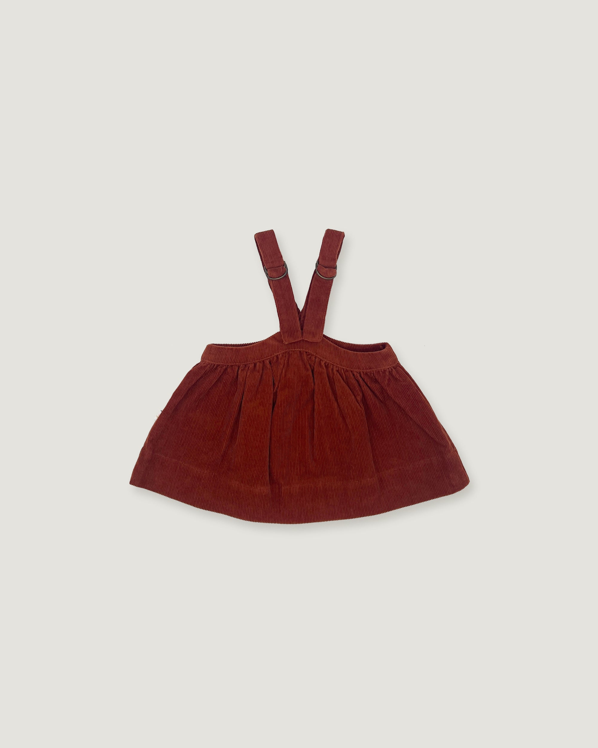 A dark reddish-brown corduroy baby or toddler pinafore skirt with adjustable shoulder straps, laid flat on a light gray background.
