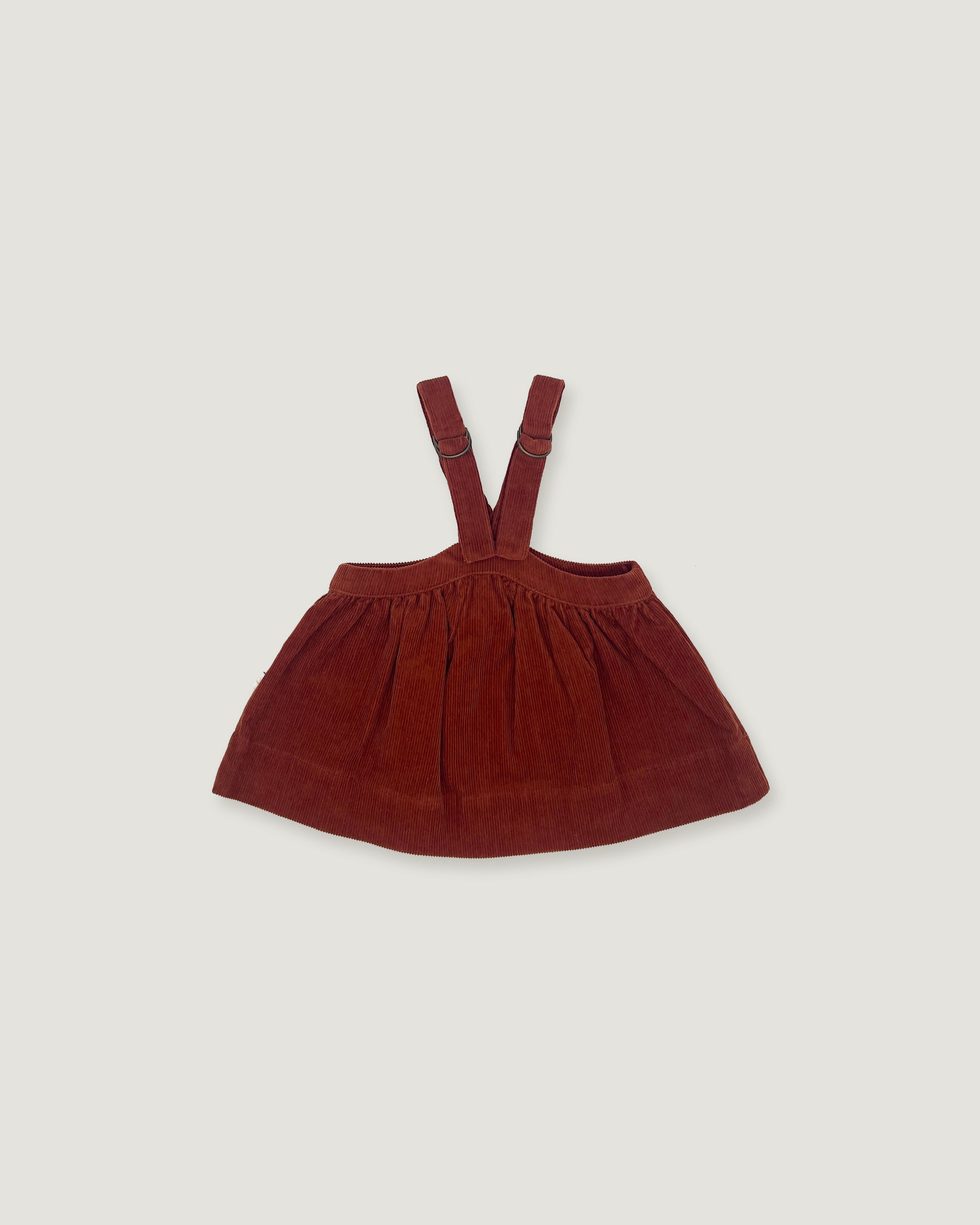 A dark reddish-brown corduroy baby or toddler pinafore skirt with adjustable shoulder straps, laid flat on a light gray background.