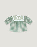 A baby girl's short-sleeve button-up shirt in a green and white gingham check pattern, featuring a wide white ruffled collar with a white cross-front bow, displayed flat against a light beige background.
